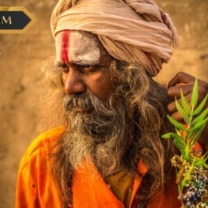 Un uomo anziano con capelli lunghi e barba, che indossa una tunica arancione e un turbante, tiene in mano una pianta frondosa. La sua fronte è segnata da vernice bianca e rossa. L'immagine presenta un'etichetta "PREMIUM", il logo "sbs viaggi" e un'etichetta Bozza automatica.