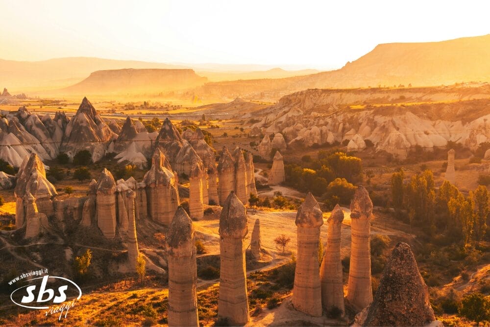 Il paesaggio illuminato dal sole della Cappadocia, in Turchia, è caratterizzato da formazioni rocciose uniche, note come camini delle fate, come una Bozza automatica naturale, incorniciata da colline ondulate e verde sparso, sotto un cielo dorato al tramonto.