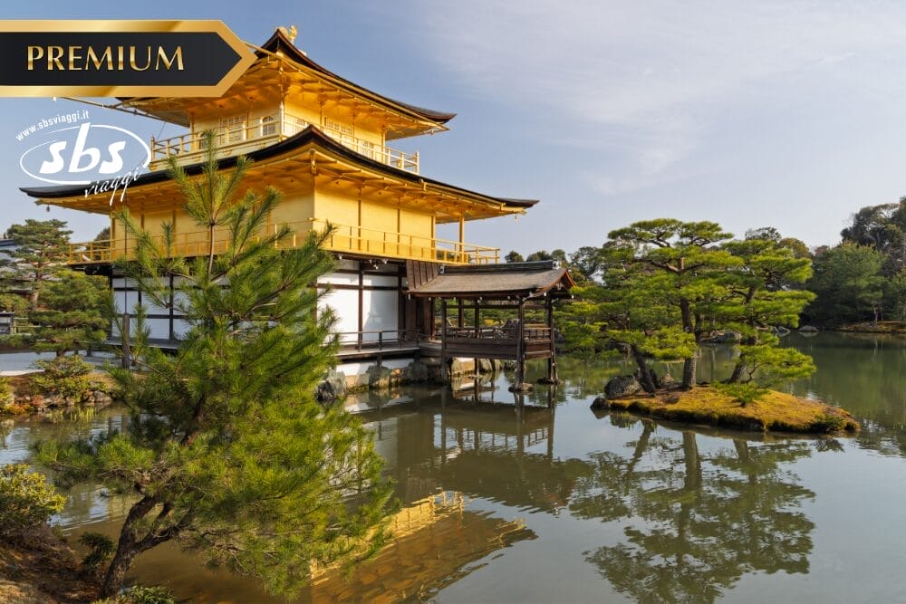 Un edificio tradizionale giapponese dorato si trova accanto a un laghetto tranquillo, circondato da alberi verdi e piccole isole. I loghi "PREMIUM", "SBS" e "Bozza automatica" sono visualizzati nell'angolo superiore sinistro dell'immagine.