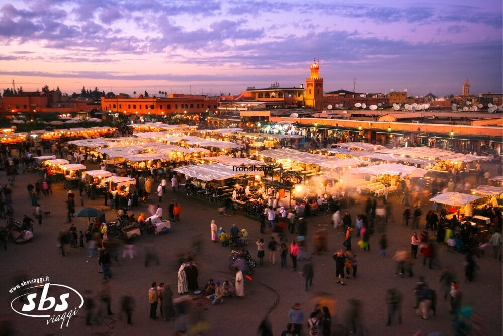 Un vivace mercato notturno nella piazza Jemaa el-Fnaa di Marrakech, nel cuore della Città imperiale del Marocco, si riempie di persone e di bancarelle luminose sotto il cielo colorato della sera e l'alto minareto di una moschea durante la Pasqua.
