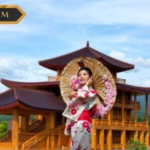 Una donna con un kimono floreale regge un ombrellino decorativo e sorride davanti a un grande edificio in legno con i tetti curvi - che cattura il fascino di Bozza automatica - incastonato tra le colline verdi e il cielo azzurro.