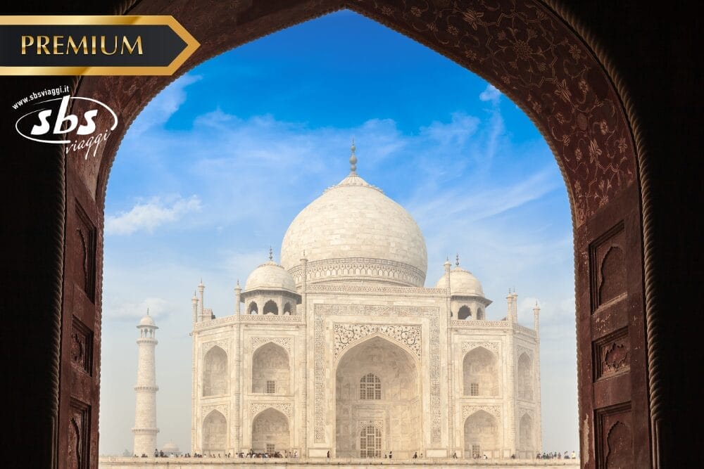 Veduta del Taj Mahal incorniciato da un portale ad arco, con un cielo blu sullo sfondo. L'immagine riporta le diciture "PREMIUM", "sbs swagat" e Bozza automatica nell'angolo in alto a sinistra.