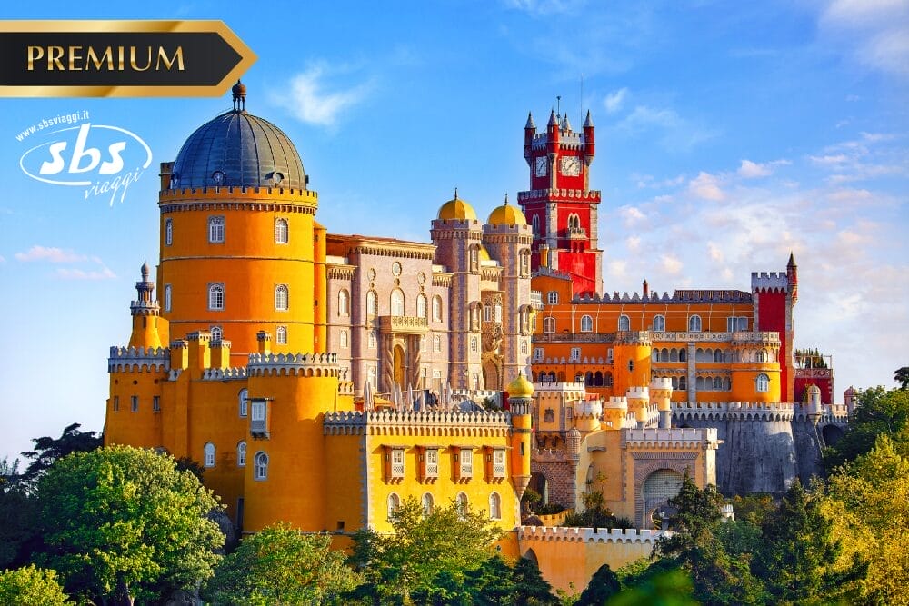 Palazzo colorato con torri gialle, rosse e rosa immerse in alberi verdi sotto un cielo blu, con la scritta "PREMIUM" in un banner dorato, il logo "sbs viaggi" in alto a sinistra e la dicitura Bozza automatica.