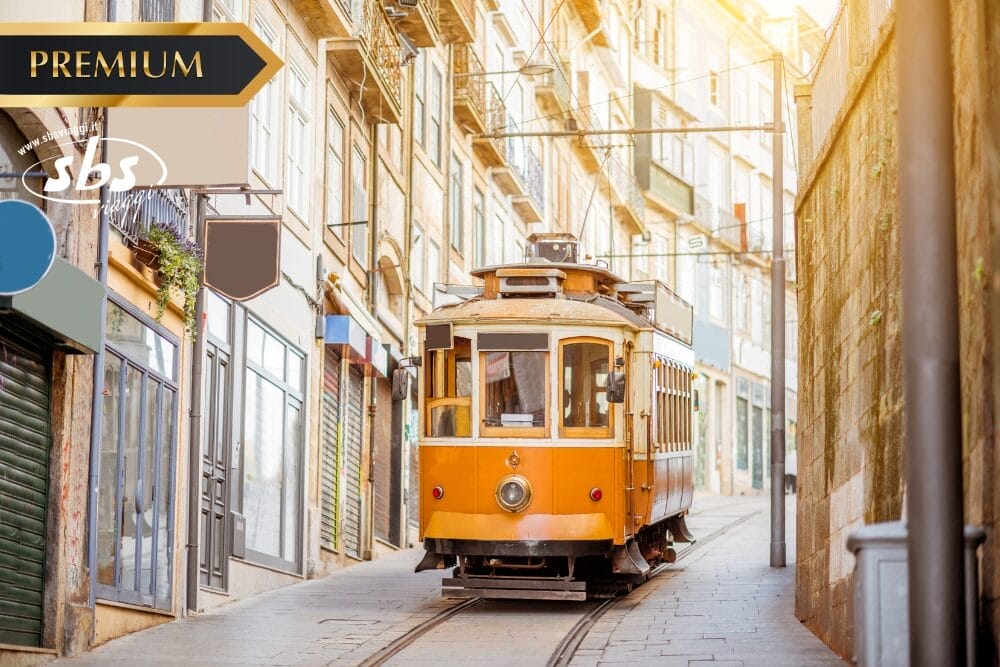 Un tram giallo d'epoca percorre una strada stretta e illuminata dal sole, fiancheggiata da vecchi edifici in una città europea. I cartelli sull'immagine recitano "PREMIUM", "sbs" e "Bozza automatica".