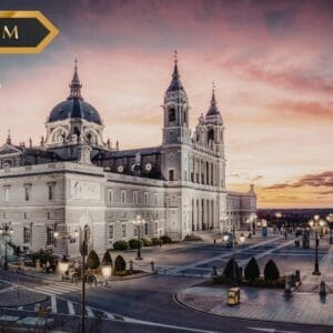 Una grande cattedrale storica di Toledo al tramonto, illuminata da luci calde, con persone che passeggiano nella piazza. Un banner "PREMIUM" e il logo dell'agenzia di viaggi "sbs viaggi" sono sovrapposti all'immagine.