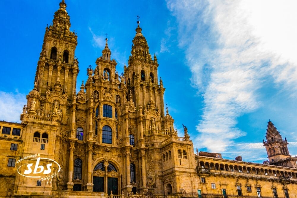 La facciata ornata della Cattedrale di Santiago de Compostela, in Spagna, si staglia su un cielo blu brillante con nuvole sparse. Questo storico edificio in pietra è caratterizzato da alte torri, intricati dettagli architettonici e vanta uno splendido design di bozza automatica.