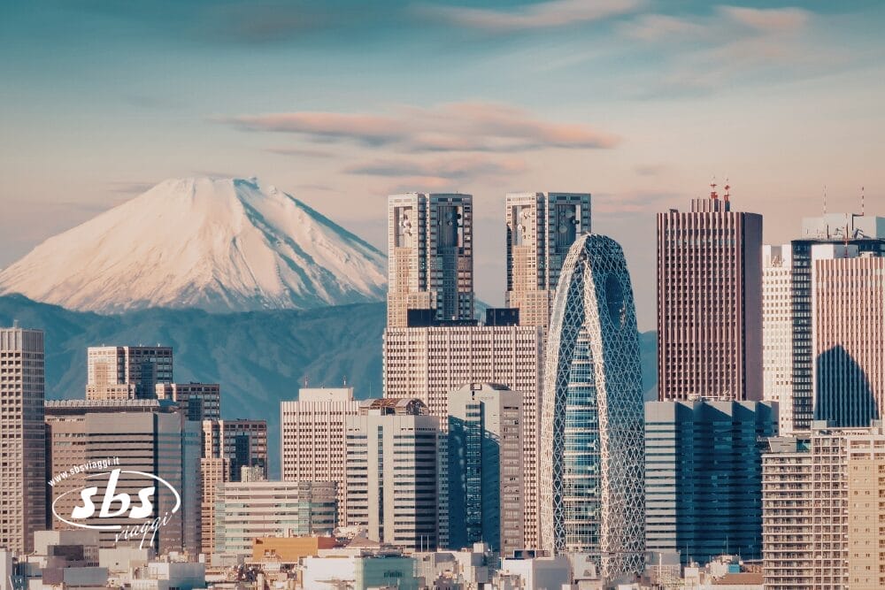 Il paesaggio di Tokyo con i moderni grattacieli in primo piano e il monte Fuji innevato sullo sfondo sotto un cielo parzialmente nuvoloso, perfetto per un tour in libertà alla scoperta delle meraviglie del Giappone.