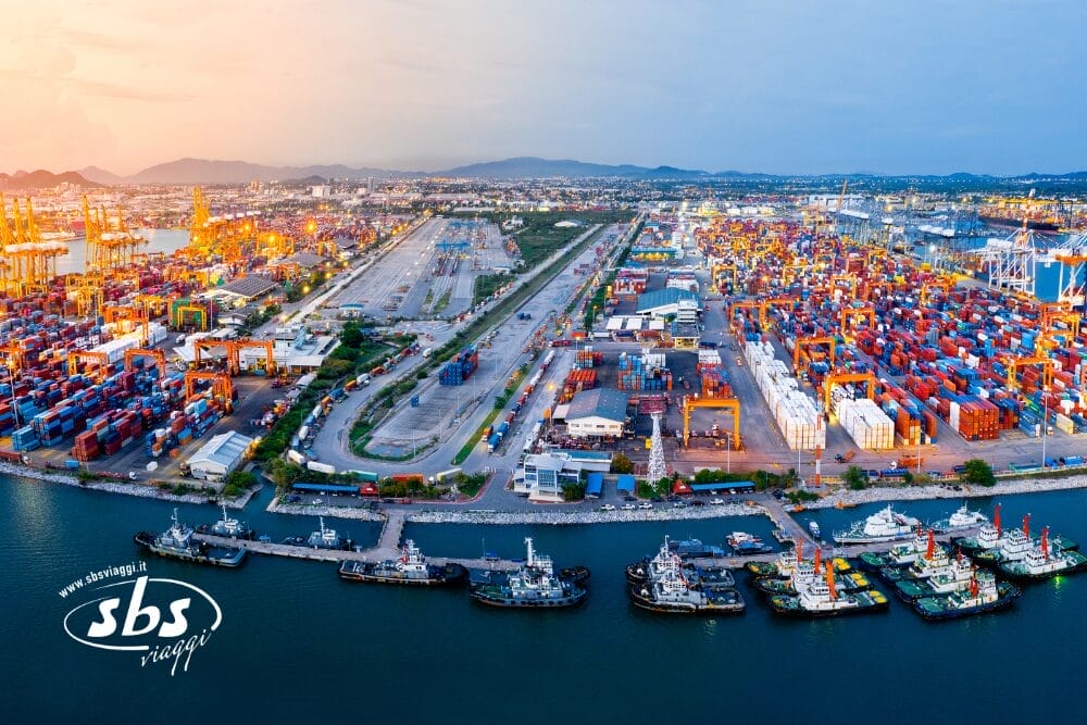 Veduta aerea di un grande e trafficato porto con container e gru colorate, che mostra la vivace economia e la forza industriale che contribuiscono a Le Meraviglie del Portogallo; le montagne e il paesaggio urbano formano uno sfondo mozzafiato.