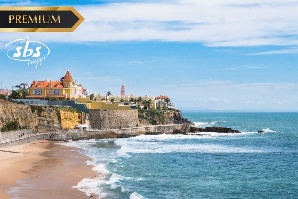 Una vista costiera panoramica con spiaggia sabbiosa, onde blu dell'oceano ed edifici storici in cima alle scogliere sotto un cielo limpido. I loghi "PREMIUM", "sbs viaggi" e "Bozza automatica" appaiono nella parte superiore dell'immagine.