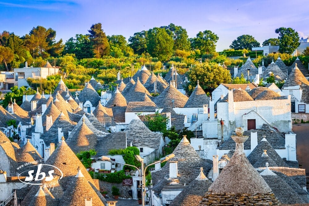 Un gruppo di trulli tradizionali con tetti conici in pietra ad Alberobello, in Italia, circondati dal verde e immersi in una calda luce solare: una tappa obbligata del Gran Tour Puglia prima di avventurarsi nella vicina Matera.