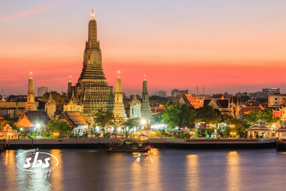 Il tempio Wat Arun di Bangkok, in Thailandia, è splendidamente illuminato al tramonto, con un cielo vibrante di arancione e rosa che si riflette sul fiume. Il vivace paesaggio urbano circonda il tempio in una scena colorata, come una bozza automatica di bellezza urbana perfettamente catturata.