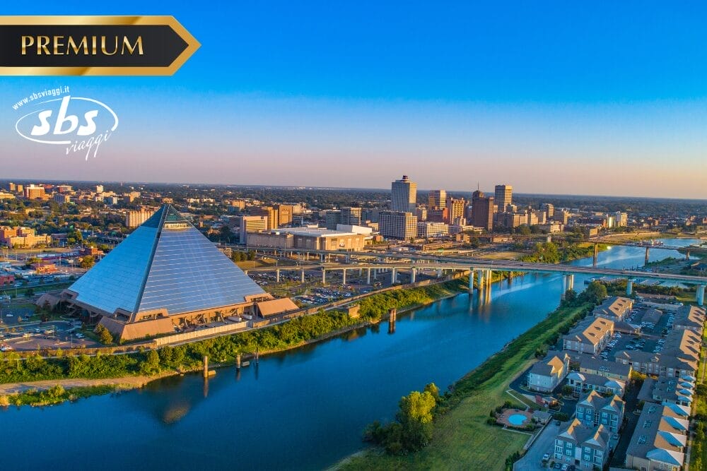 Veduta aerea del centro di Memphis, Tennessee, con la piramide di vetro Bass Pro Shops lungo il fiume Mississippi. Sullo sfondo appaiono gli edifici della città e un ponte. I loghi "Premium", "sbs viaggi" e "Bozza automatica" sono sovrapposti.