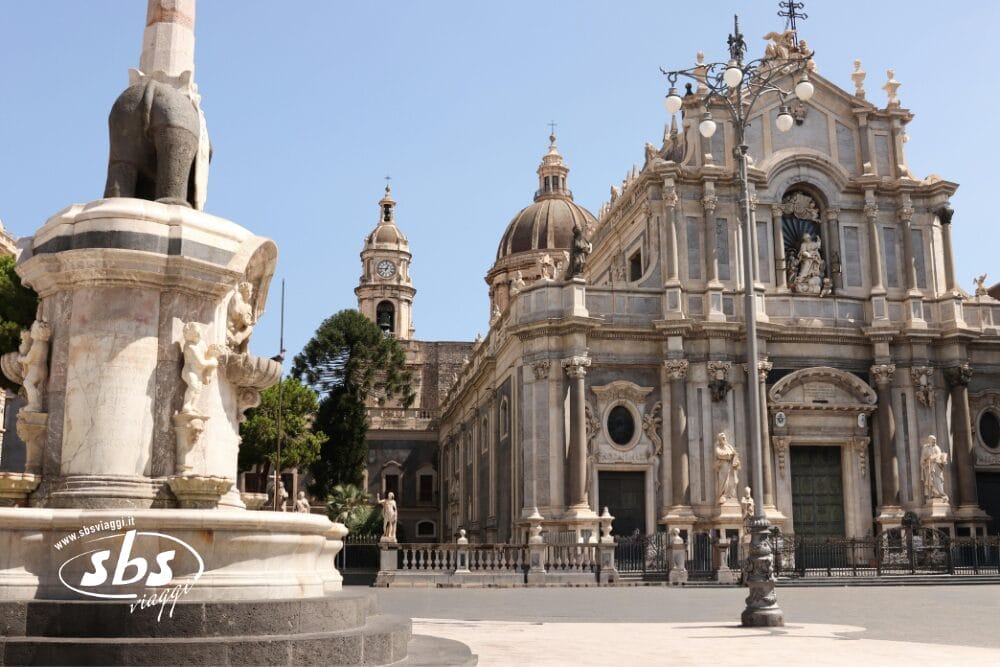 Una piazza storica di Concordia Sicilia con una cattedrale barocca ornata, statue in pietra e una fontana con una statua di elefante. Il cielo limpido e l'area calma e vuota invitano a fare un giro tranquillo in questo luogo affascinante.