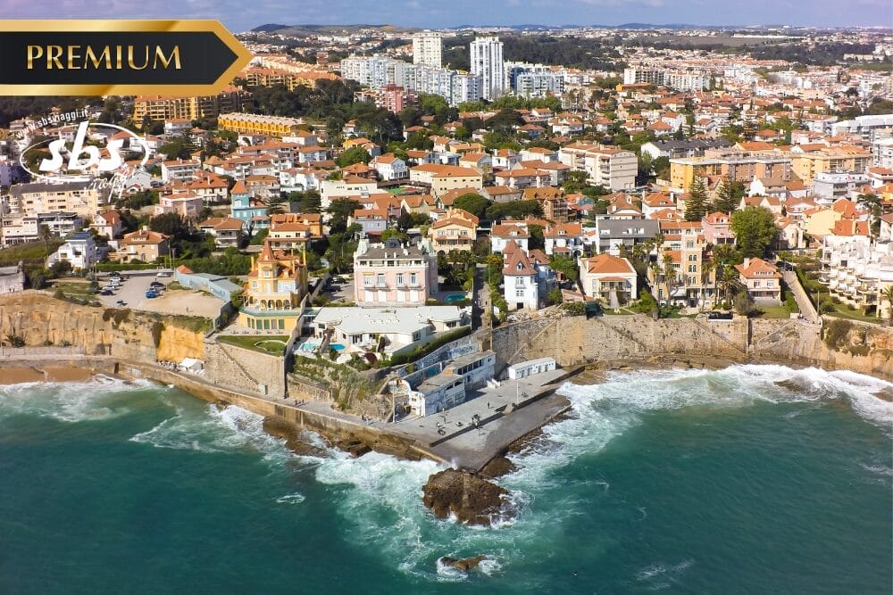 Veduta aerea di una città costiera di Portogallo con case colorate, condomini e un litorale roccioso. Le onde si infrangono sulla riva e nell'angolo in alto a sinistra compare il banner "Premium".
