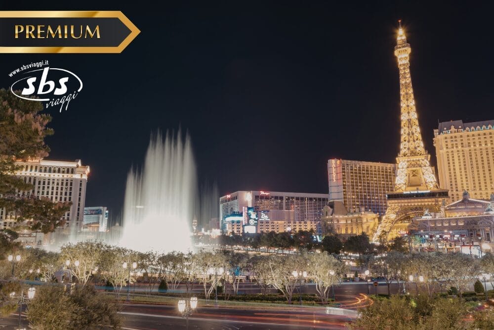Vista notturna della Strip di Las Vegas con gli hotel illuminati, la replica della Torre Eiffel e le fontane del Bellagio. I loghi "Premium", "sbs viaggi" e "Bozza automatica" sono visualizzati nell'angolo in alto a sinistra.