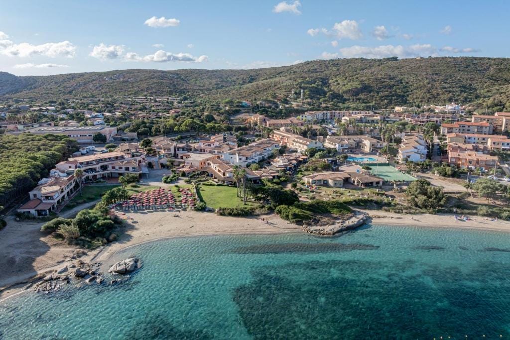 Veduta aerea di una località balneare con spiagge sabbiose, acque turchesi limpide, lettini con ombrelloni e gruppi di edifici circondati dal verde e dalle colline: l'ideale per rilassarsi o lavorare alla prossima Bozza automatica.