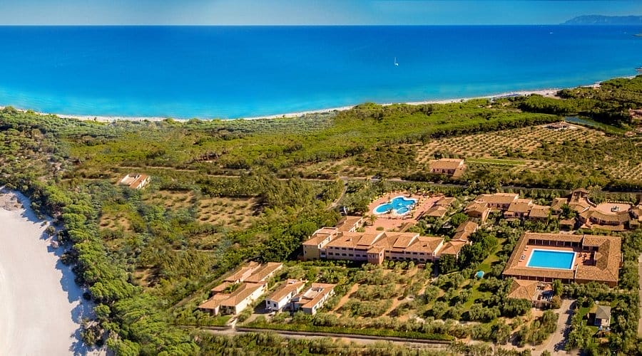 Vista aerea di un resort balneare con piscine, giardini e diversi edifici immersi nel verde, vicino a un'ampia spiaggia sabbiosa e a un mare cristallino sotto un cielo luminoso: la vostra perfetta fuga automatica Bozza.
