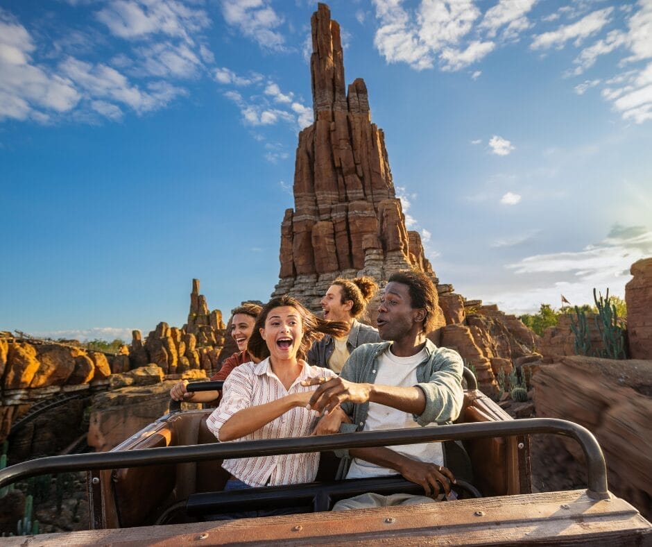 Quattro persone salgono sulle montagne russe attraverso un paesaggio a tema desertico a Disneyland Paris, sorridendo e ridendo mentre provano il brivido sotto un cielo azzurro: ogni Soggiorno con Ingresso al Parco è indimenticabile.