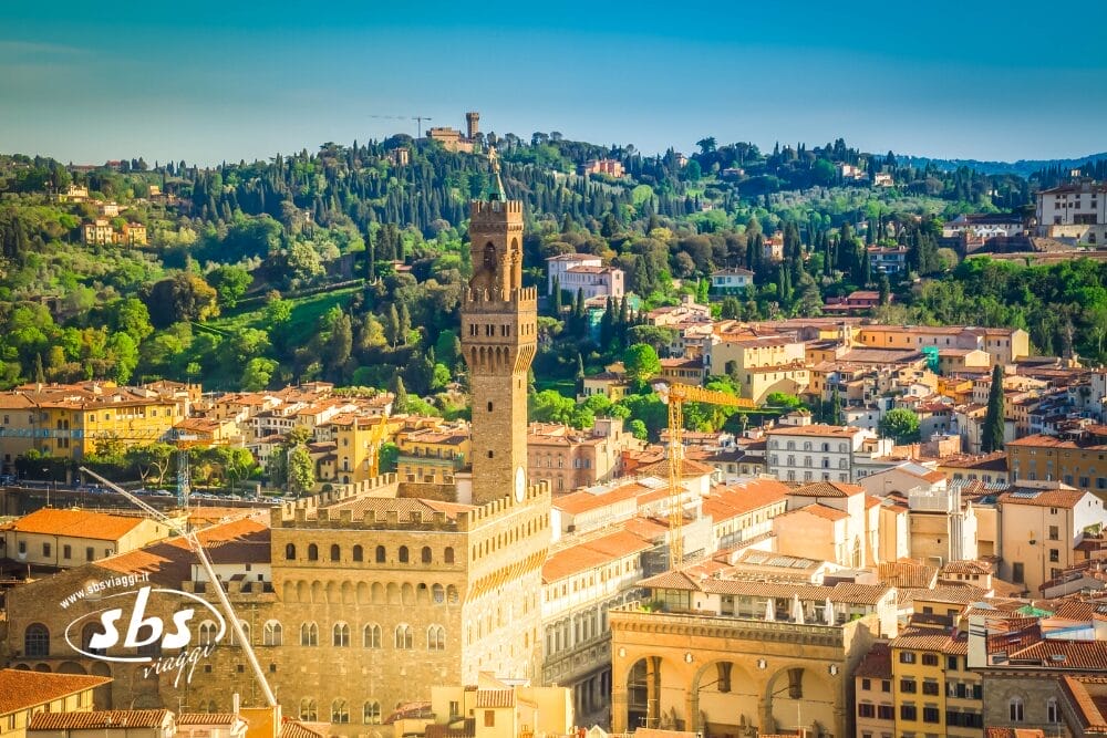 Una vista panoramica di Firenze, Italia, con la storica torre di Palazzo Vecchio circondata da edifici dai tetti arancioni e colline verdeggianti sotto un cielo azzurro e limpido, che evoca la bellezza senza tempo di Parigi e dei Castelli della Loira.