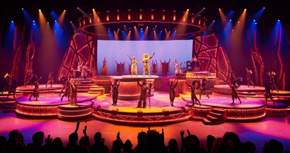 Un grande palcoscenico con attori in costumi elaborati, una vibrante illuminazione arancione e gialla e un pubblico festante dà il benvenuto agli ospiti di Disneyland Paris. Fondali drammatici e piattaforme circolari creano un'atmosfera teatrale e vivace, perfetta per qualsiasi soggiorno.