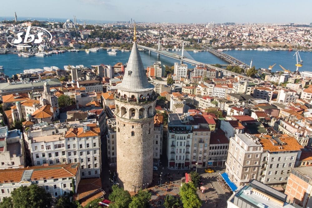 Veduta aerea di Istanbul con la storica Torre di Galata e gli edifici della città, con il Bosforo, un ponte e un cielo limpido sullo sfondo.