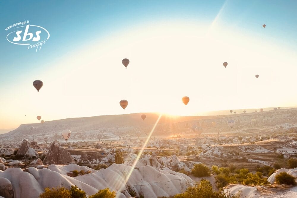 Diverse mongolfiere fluttuano sopra un paesaggio roccioso e illuminato dal sole all'alba o al tramonto, con un morbido bagliore dorato che illumina la scena, come una bozza automatica che cattura l'arte della natura tra le formazioni rocciose uniche.