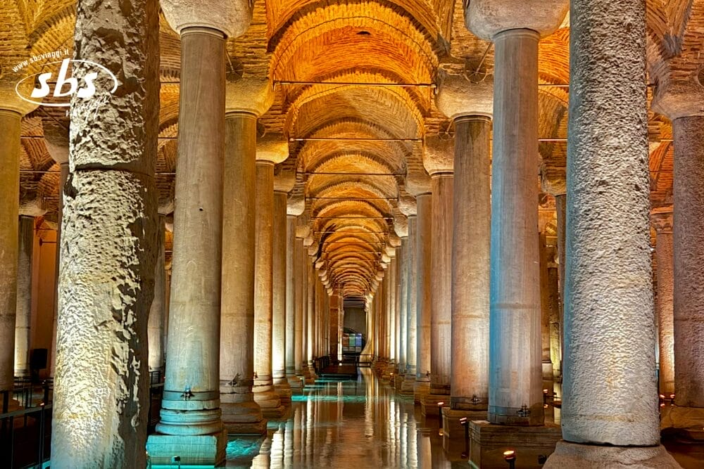 File di alte e antiche colonne di pietra con soffitti ad arco sono illuminate drammaticamente con luci gialle e blu, i cui riflessi scintillano in una piscina poco profonda: una scena incantevole all'interno di questa storica struttura sotterranea, catturata come Bozza automatica.