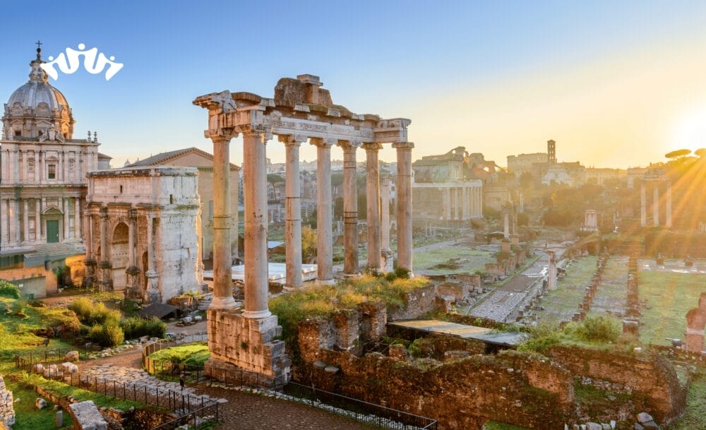 Antiche rovine romane con alte colonne e pietre sparse si ergono sotto il cielo terso dell'alba. Un edificio a cupola si trova sulla sinistra, la luce del sole bagna la scena d'oro - perfetta per iniziare la vostra crociera a Civitavecchia o per esplorare con MSC World Asia. Una piccola icona bianca a forma di corona si trova nell'angolo in alto a sinistra.