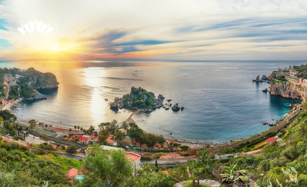 Una vista panoramica di un paesaggio costiero al tramonto, con acque azzurre e calme, isolotti rocciosi, verde lussureggiante, case sparse e un cielo drammatico, che cattura la serena bellezza spesso ammirata su una Crociera Mediterraneo da Civitavecchia.